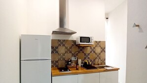 A compact kitchen with a refrigerator, microwave, and a stove hood.