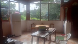 Una habitación con mesa de comedor, sillas, refrigerador y ventanas amplias que dan a vistas de follaje.