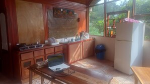 Una cocina compacta con armarios de madera, una encimera, un lavabo, una estufa, un refrigerador y un ordenador portátil sobre una mesa.