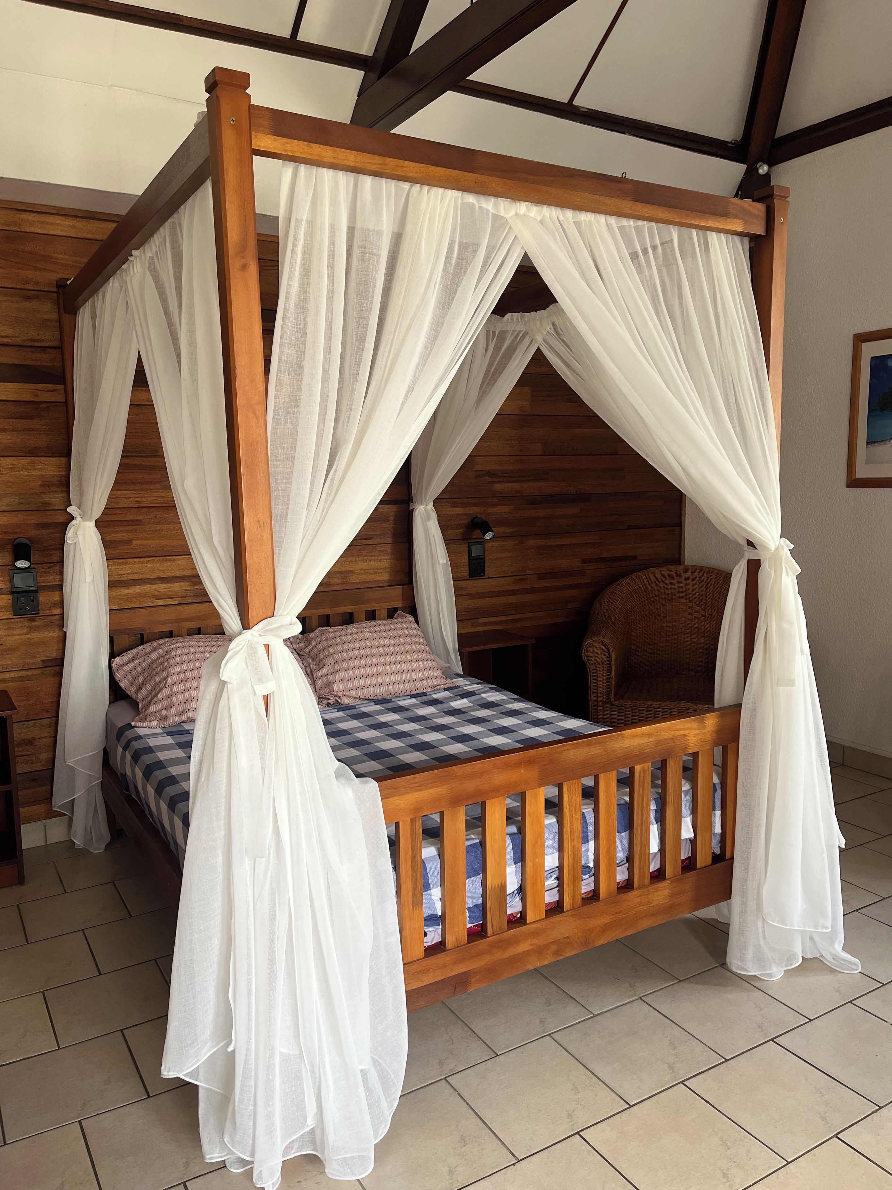 A four-poster bed with white drapes, wooden headboard, and a checkered bedspread.