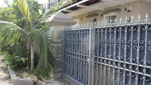 Un espace clos, délimité par une clôture en métal, avec un palmier et un bâtiment doté d’un balcon.