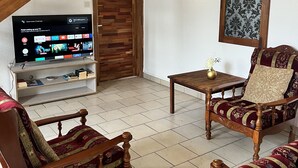 Un salon comprenant un meuble TV en bois, deux fauteuils à motifs, une petite table en bois et un élément décoratif mural.