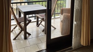 Un balcon avec une table et des chaises, une vue sur les immeubles et les arbres, et une porte-fenêtre coulissante.