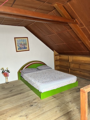 Une petite chambre avec un lit simple, un plafond en pente et des poutres en bois.
