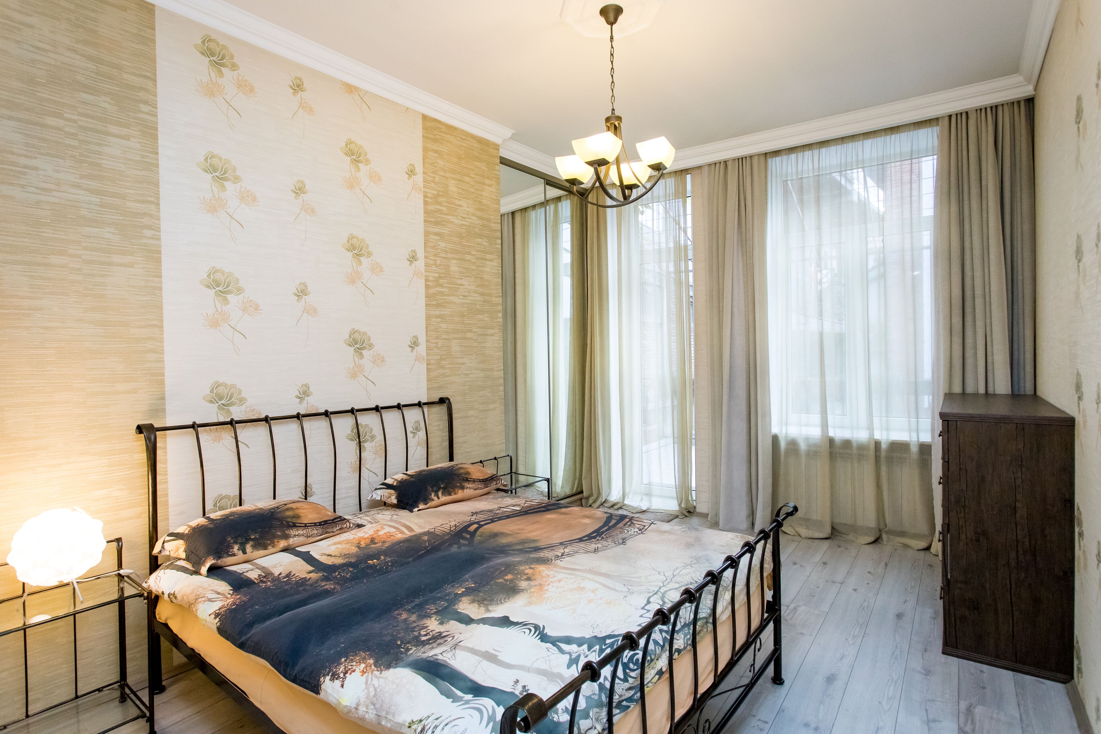 Une chambre à coucher comprenant un lit, une table de chevet, une armoire en bois et une grande fenêtre avec des rideaux.