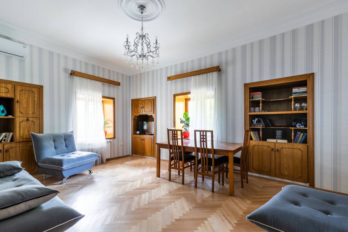 A living room with a sofa, a dining table with chairs, a chandelier, and wooden cabinets.