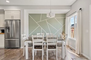 Cozinha moderna com geladeira de aço inoxidável, mesa de jantar com cadeiras brancas e design geométrico na parede.