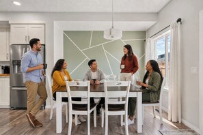 A modern kitchen with white cabinets, a stainless steel refrigerator, and a dining area with a white table and chairs.