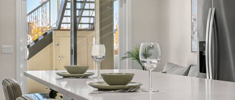 A modern kitchen with a white countertop, two green bowls, and two wine glasses.