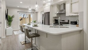 A modern kitchen with a central island, stainless steel appliances, pendant lighting, and a view to the outside. - 1BR Walk Out Suite » Backyard » Patio » 65” TV (Calgary)