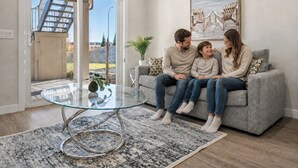 A living room with a glass coffee table, a grey sofa, and a large painting on the wall. - 1BR Walk Out Suite » Backyard » Patio » 65” TV (Calgary)