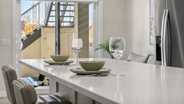 A modern kitchen with a white countertop, two green bowls, and two wine glasses. - 1BR Walk Out Suite » Backyard » Patio » 65” TV (Calgary)