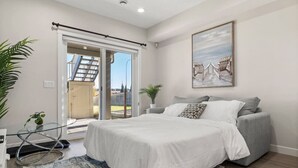 A bedroom with a bed, a grey sofa, a glass table, and a large window with a view of a building. - 1BR Walk Out Suite » Backyard » Patio » 65” TV (Calgary)