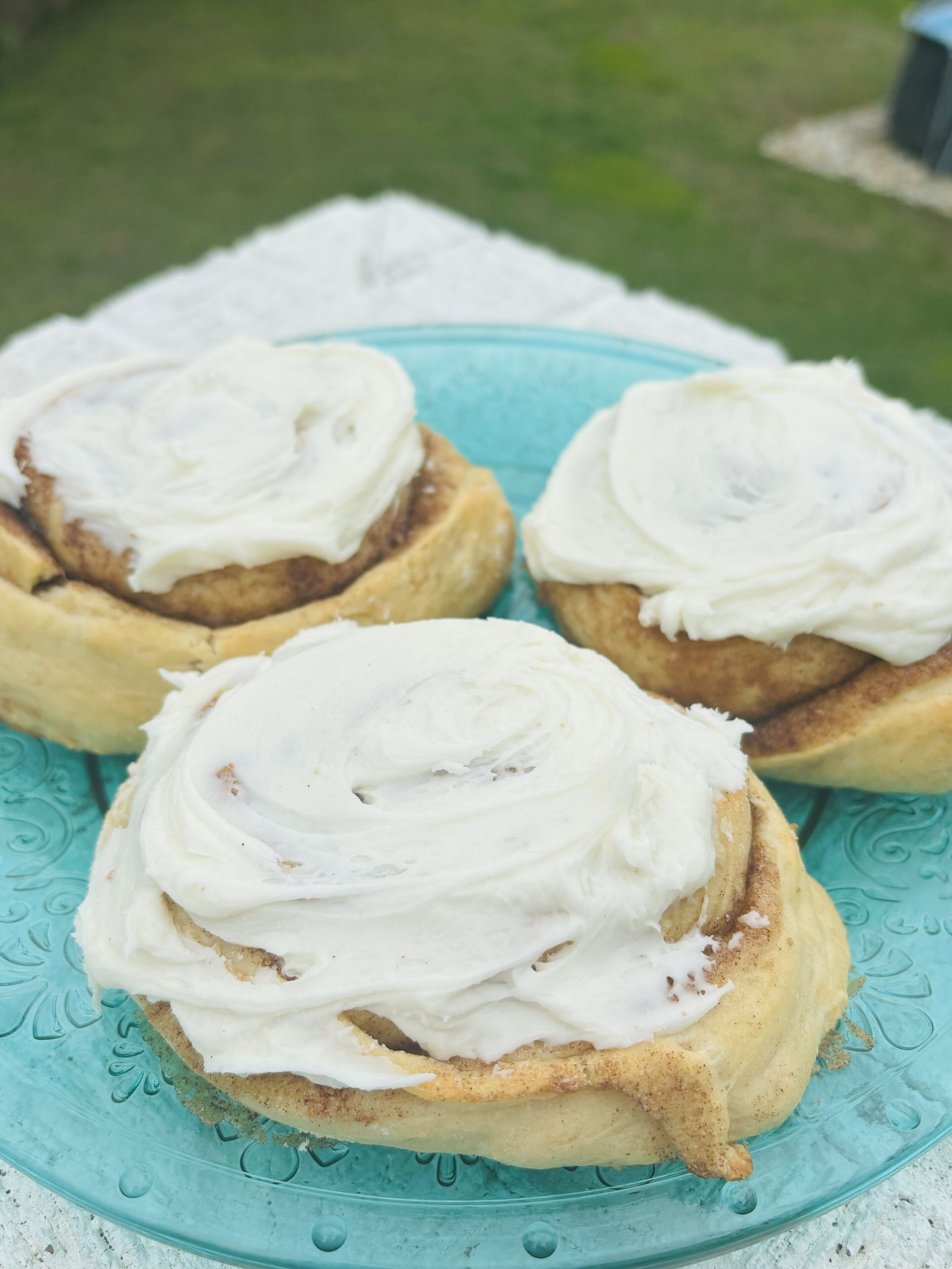 Tres rollos de canela con glaseado blanco sobre un plato turquesa.