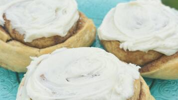 Tres rollos de canela con glaseado blanco sobre un plato turquesa.