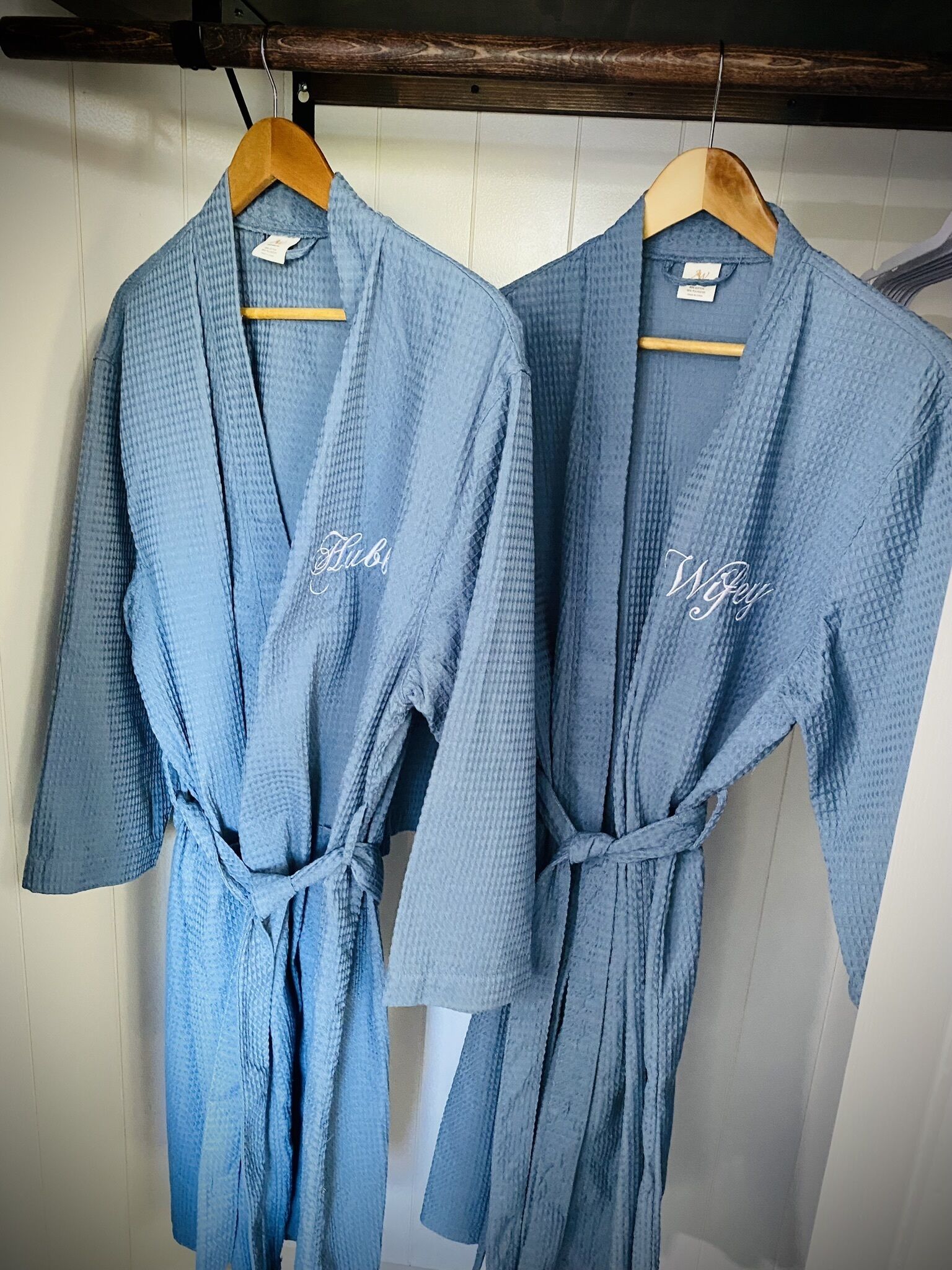 Deux robes bleues sont suspendues à des cintres en bois contre un mur blanc.