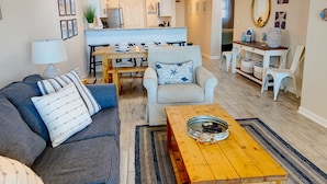 Ein Wohnzimmer mit einer Couch, einem Sessel, einem Couchtisch und einem Essbereich mit Tisch und Stühlen.