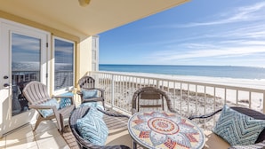 Ein Balkon mit Korbstühlen und einem Mosaik-Tisch, mit Blick auf einen Strand.
