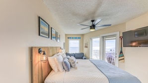 Ein Schlafzimmer mit einem großen Bett, einem Deckenventilator, einem an der Wand befestigten Fernseher und Blick auf den Balkon.