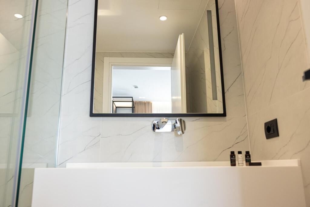 Un baño moderno con pared de mármol, un espejo grande y un lavabo blanco.
