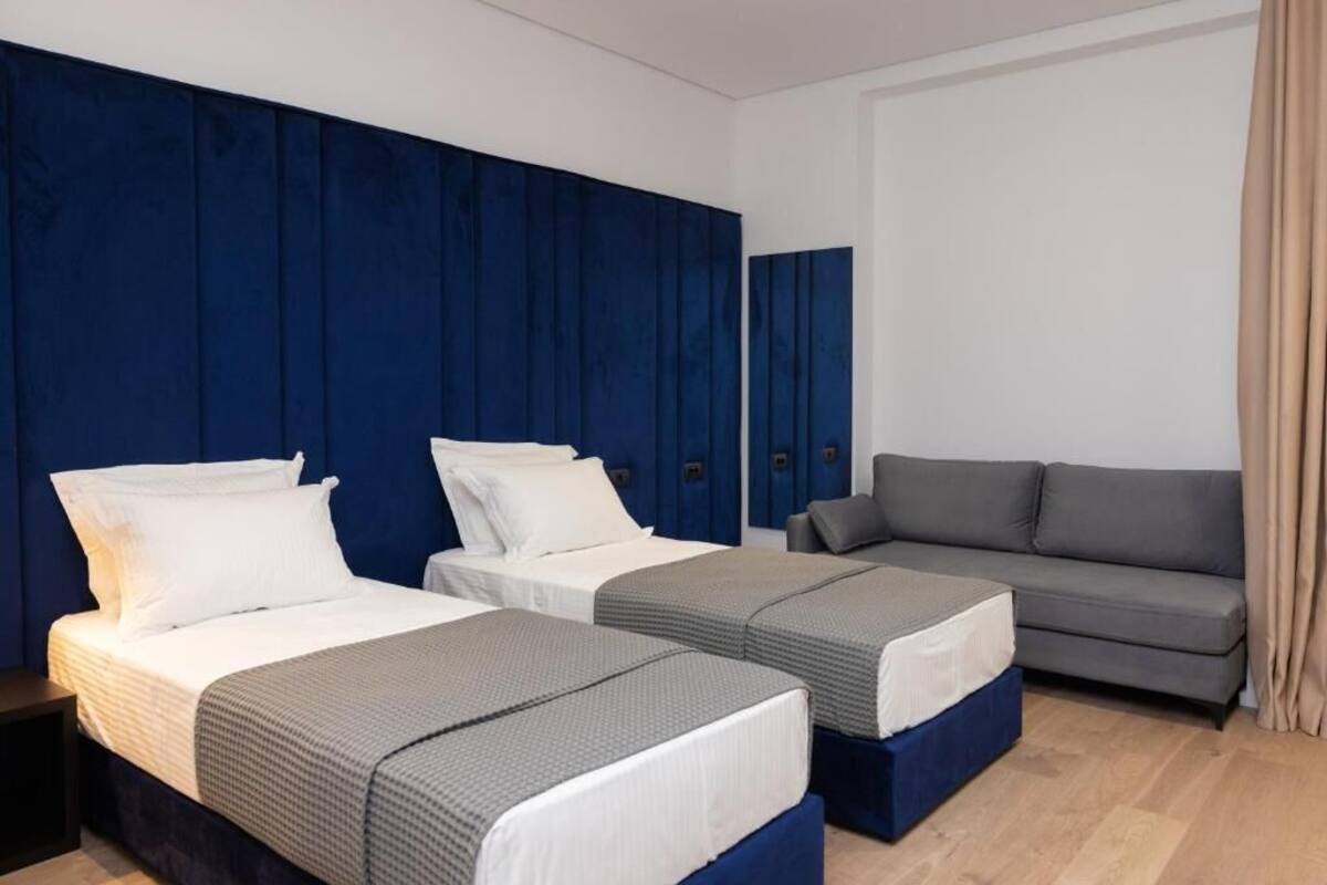 A hotel room with two beds, a grey sofa, and a blue accent wall.