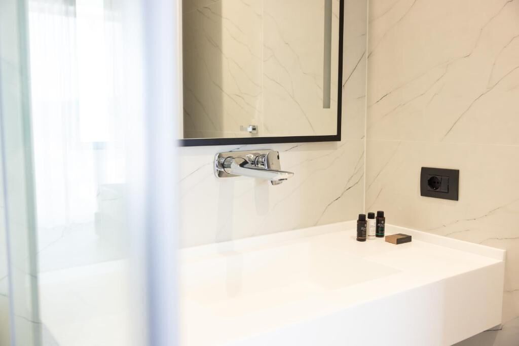 Een moderne badkamer met een witte marmeren wasbak, een grote spiegel en wat toiletartikelen op het aanrecht.