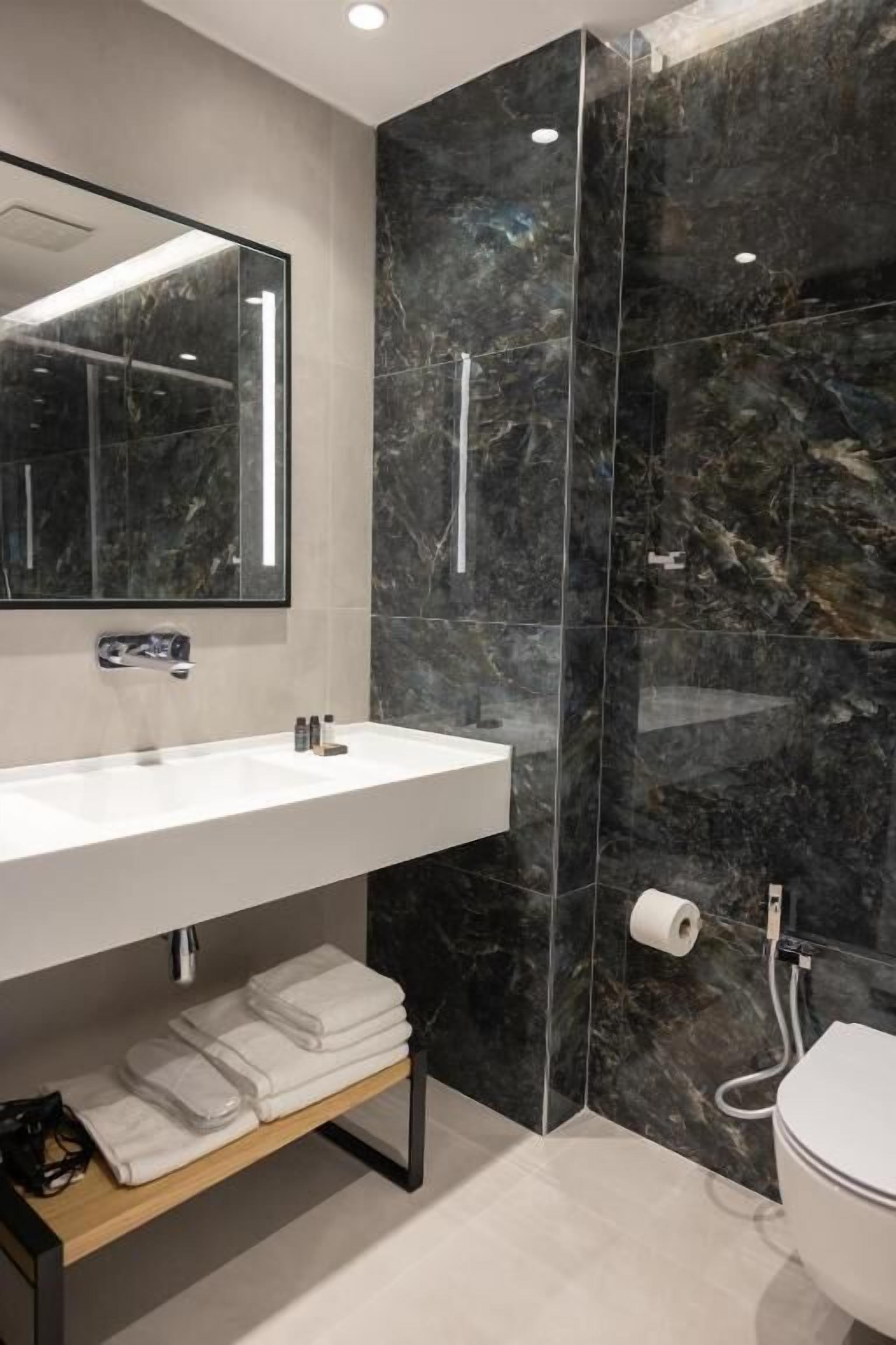 Een moderne badkamer met een marmeren wand, een witte wastafel en een toilet.