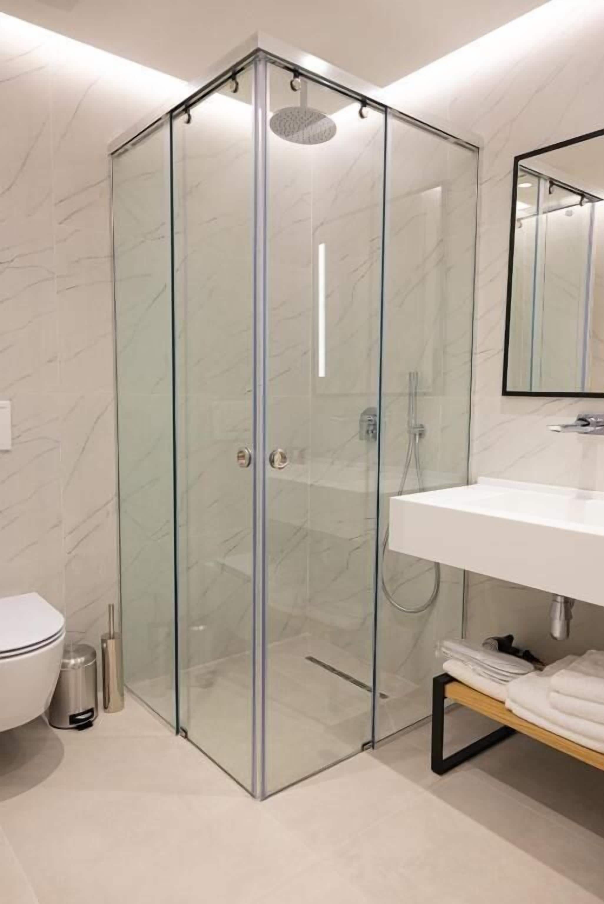A modern bathroom with a glass-enclosed shower, a white sink, and a mirror above it.