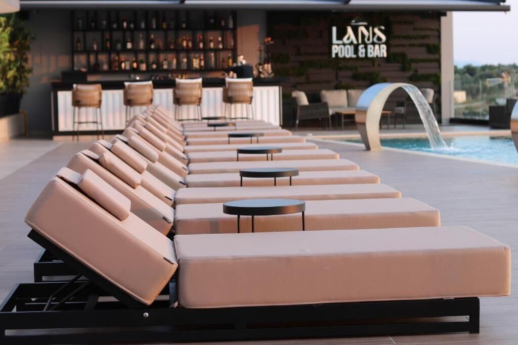 Un espace aménagé au bord de la piscine, avec des chaises longues et des tables, un bar et un panneau indiquant « LANS POOL & BAR ».