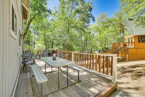 Une terrasse en bois avec une table de pique-nique et des chaises, entourée d’arbres.