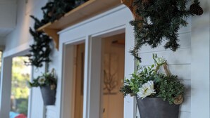 A porch with a white railing, decorated with hanging greenery and potted plants.