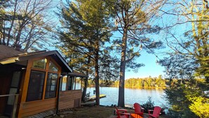 A cabin with a deck overlooking a lake, surrounded by trees.
