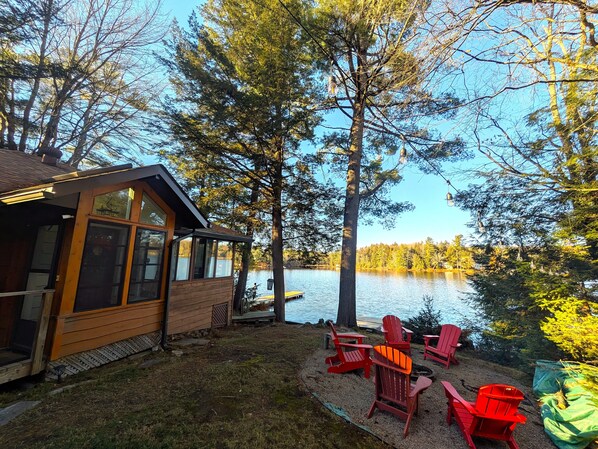 Una cabaña con terraza que da a un lago, rodeada de árboles.
