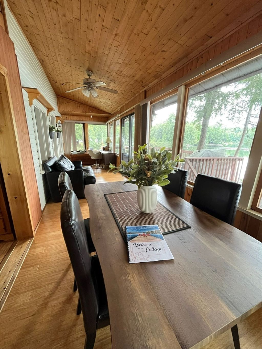 A wooden-paneled room with a large table, chairs, and a ceiling fan.