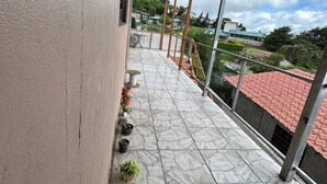 A covered balcony with stone flooring, potted plants, and a view of a red-roofed building in the background. - Ocean View (Monteverde)