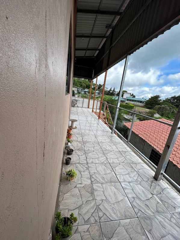 A covered balcony with stone flooring, potted plants, and a view of a red-roofed building in the background. - Ocean View (Monteverde)
