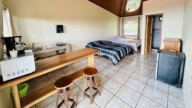 A compact room with a bed, a small table with a coffee maker, a stool, and a suitcase. - Ocean View (Monteverde)