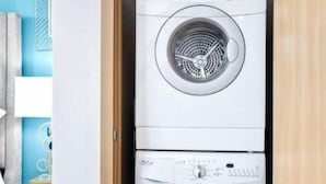 Una unidad de lavandería compacta de dos puertas en una habitación con suelo de madera y una pared azul de acento.