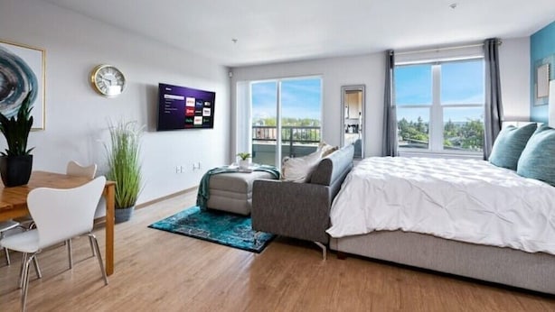 Un dormitorio moderno con una cama grande, un escritorio, una silla y un televisor en la pared.