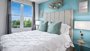 Un dormitorio con una cama grande, una ventana con cortinas, una mesita de noche con lámpara y decoración en la pared.