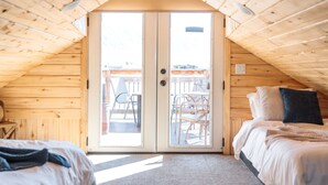 Een gezellig slaapkamer onder het dak met twee bedden, een houten plafond en een schuifdeur naar een balkon.