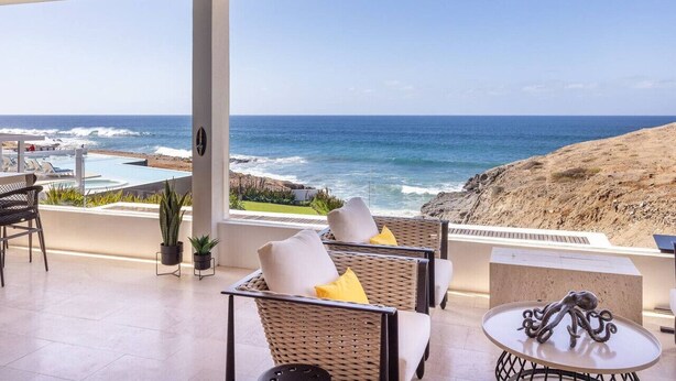 Ein Balkon mit Korbmöbeln, einem kleinen Tisch und Blick auf das Meer und den Strand.