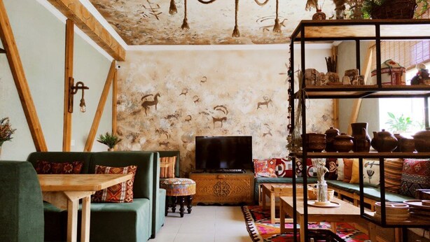A cozy living room with a sofa, coffee table, and TV stand. There is a bookshelf with decorative items and a rug on the floor. - Silkroad Guest house (Bishkek)