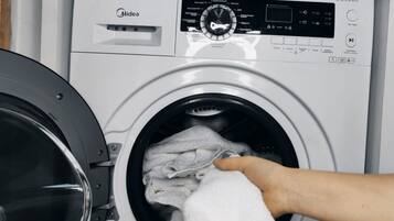 Une machine à laver à chargement frontal, dotée d’un panneau de commande, et une personne qui y place une serviette.