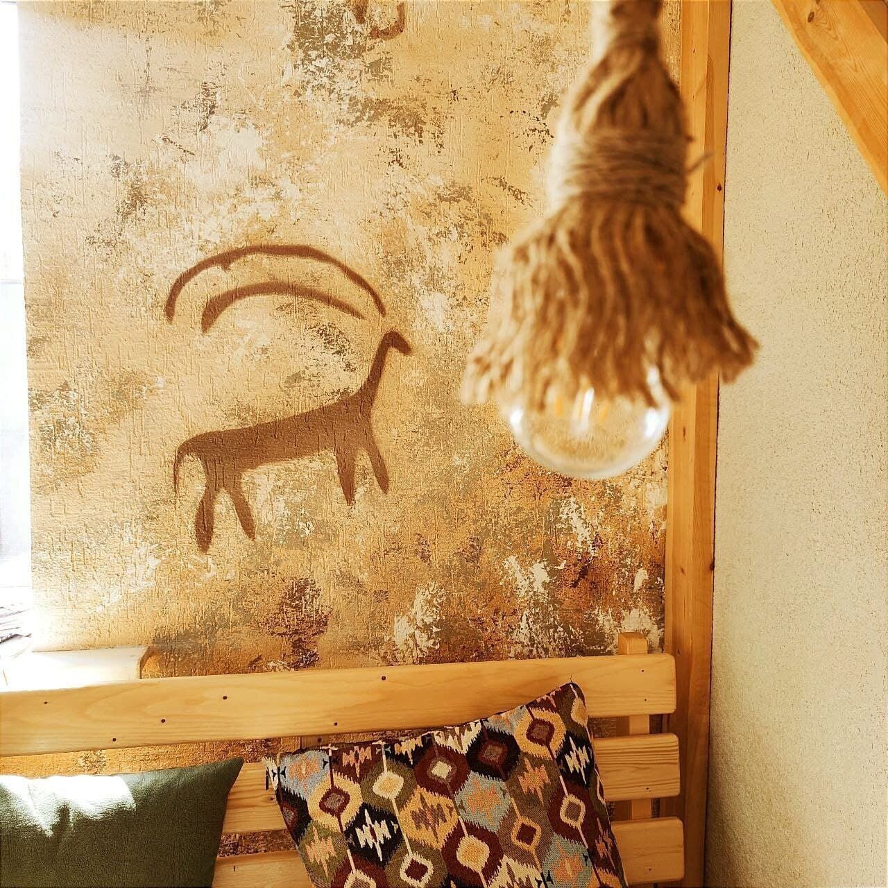 A rustic wooden bench with a patterned cushion and a wall with a goat silhouette.