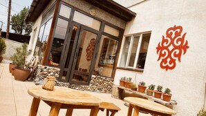 An outdoor patio with wooden tables and chairs, a stone wall, and potted plants. - Silkroad Guest house (Bishkek)