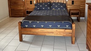 Une chambre à coucher avec un lit en bois, deux tables de chevet, une commode, un ventilateur de plafond et une armoire en bois.