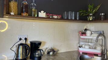 Een keuken met een marmeren aanrecht, een koffiezetapparaat, een waterkoker, een spoelbak met een afwassysteem, en diverse keukengerei en containers op de plank.