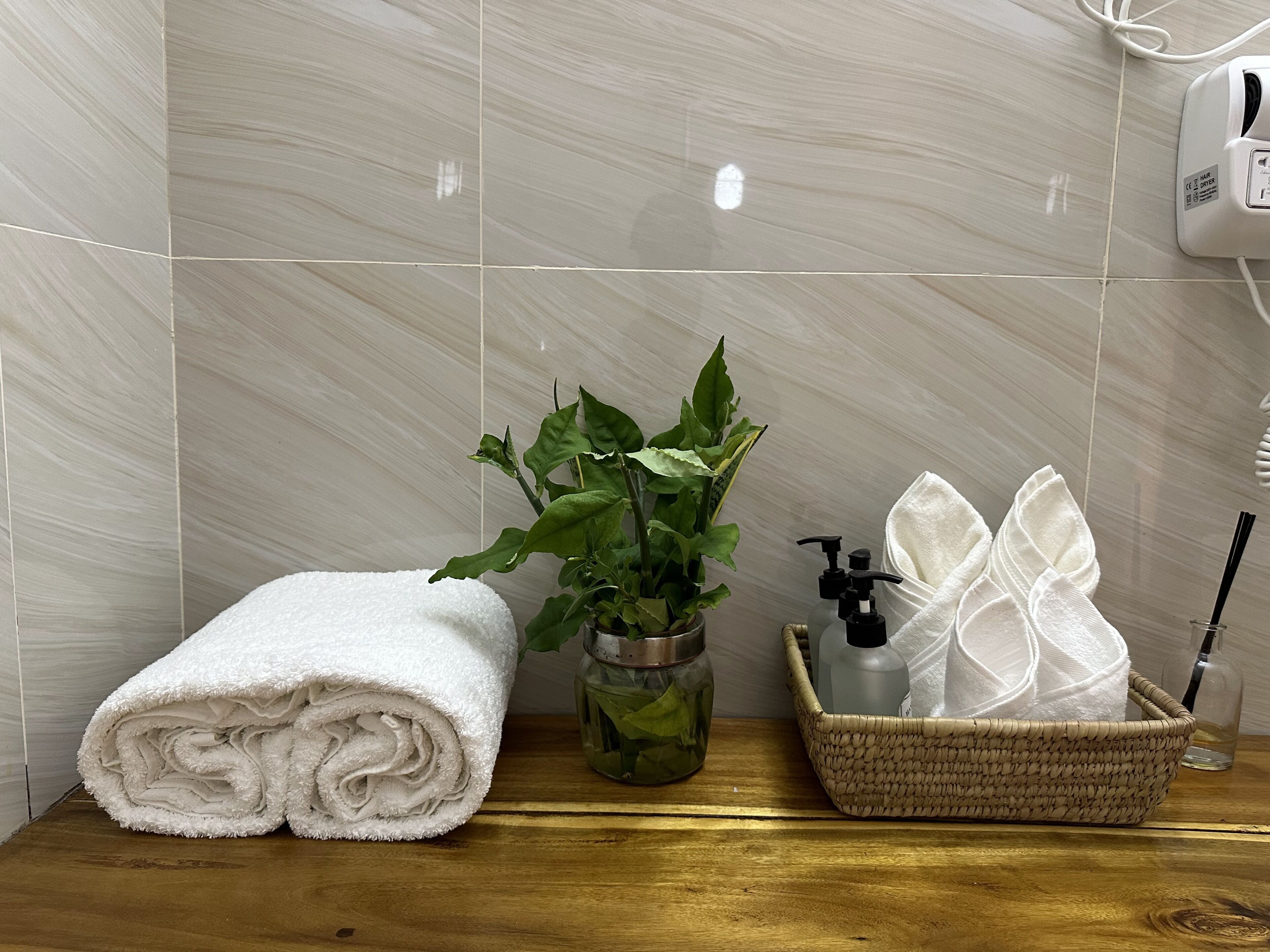 A bathroom with a white towel, a potted plant, a glass bottle, and a basket with a towel and a bottle.