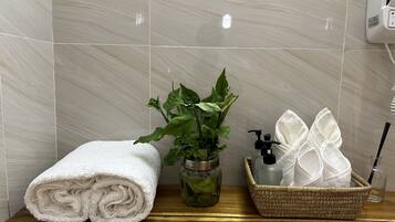 A bathroom with a white towel, a potted plant, a glass bottle, and a basket with a towel and a bottle.